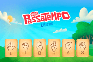 No topo em letras vermelhas o nome da marca Nestlè e da bolacha passatempo. Fundo céu azul uma árvore à direita, nuvens e sol no topo. Abaixo bolachas lado a lado uma com cada letra do alfabeto manual formando a palavra Libras. E abaixo duas crianças sinalizando. bolacha com o alfabeto manual